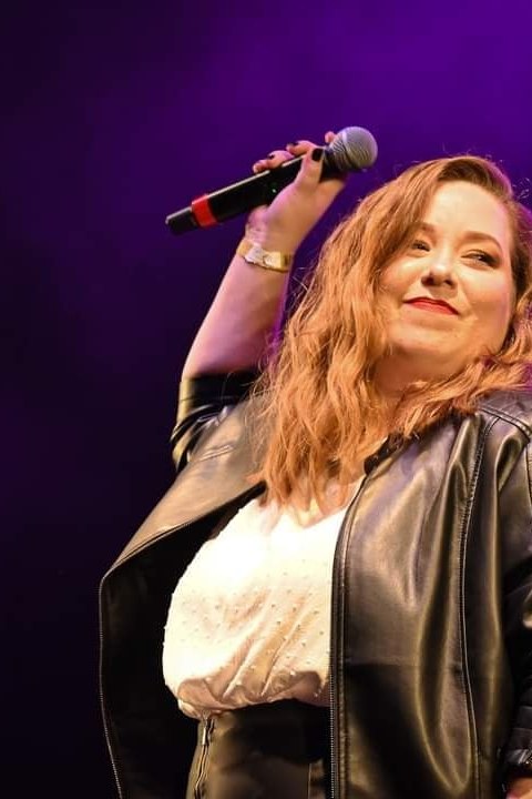 Letícia Bertoldi cantando no palco, sob luz violeta