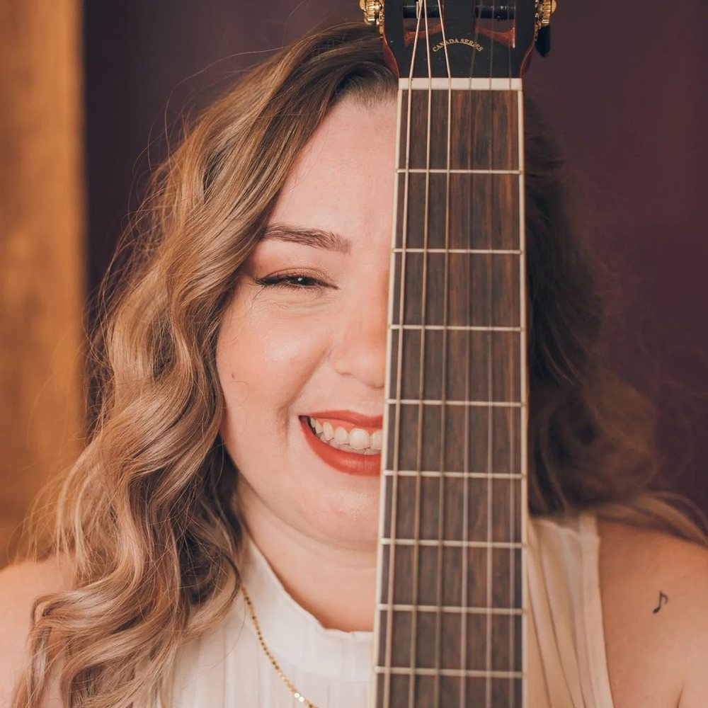 Retrato de Letícia Bertoldi sorrindo, com o braço de um violão à frente do rosto